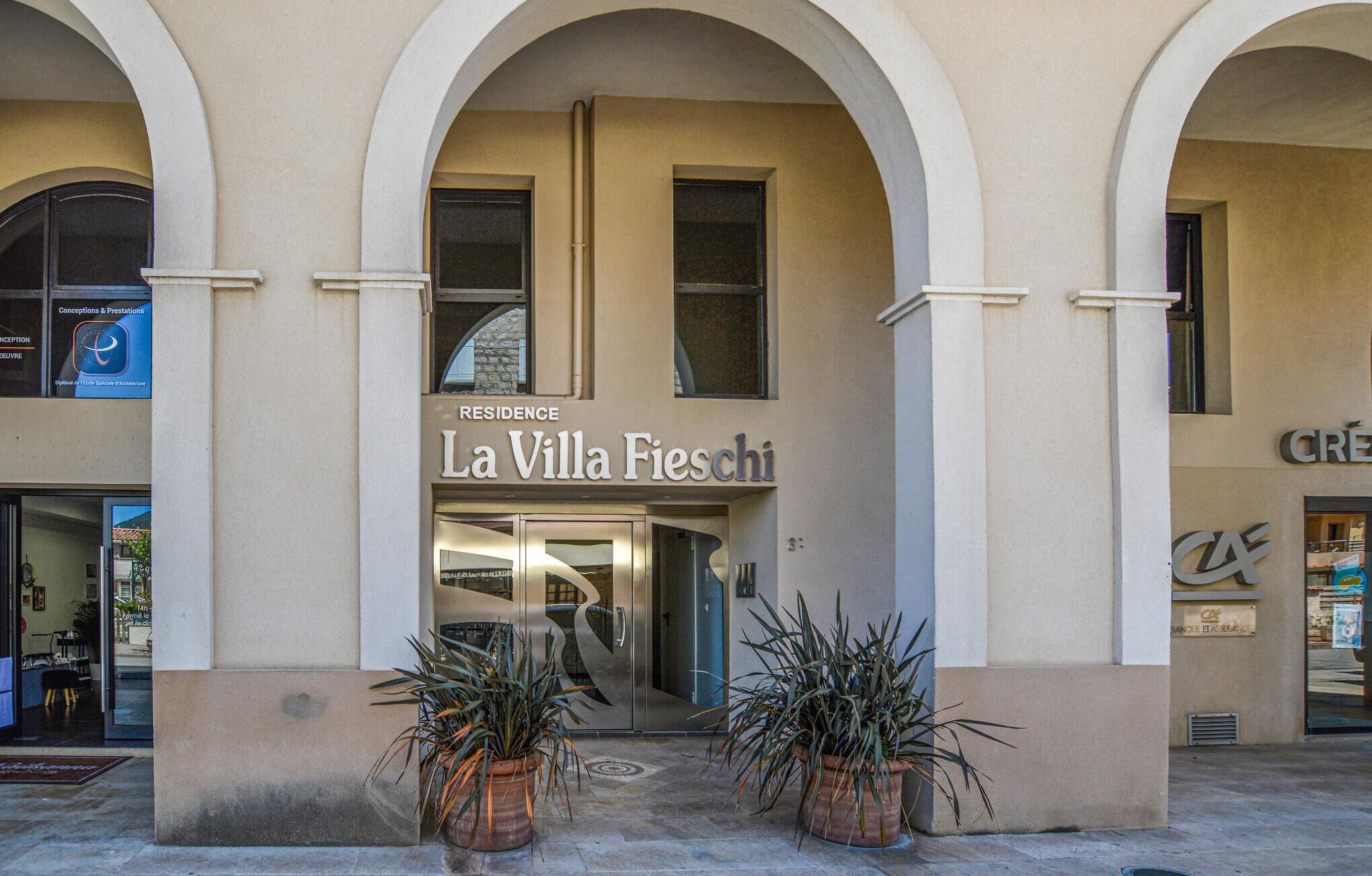 A building with a sign reading "Residence La Villa Fieschi" and an entrance with two potted plants.