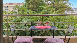 Un balcone con un tavolo e due sedie, affacciato su un giardino e degli edifici.