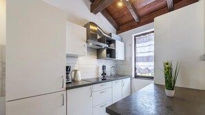 Una cocina moderna con armarios blancos, una campana extractora de acero inoxidable y un ventanal con cortinas ligeras.