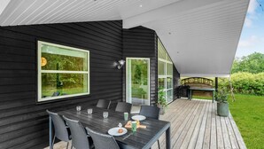 Un área de comedor exterior moderna con una terraza de madera oscura, una mesa con sillas y una pérgola.