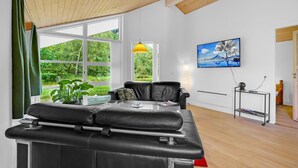 Una habitación moderna con un ventanal grande, un sofá de cuero negro, un televisor en la pared y techo de madera.
