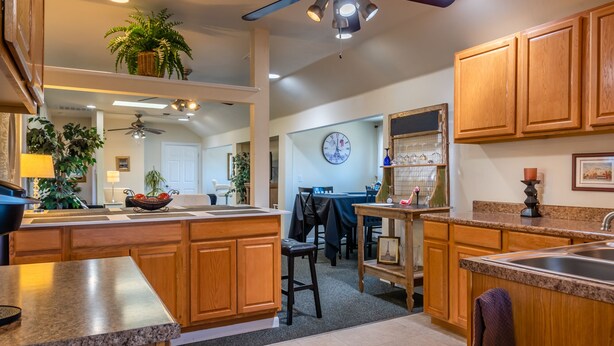 Une cuisine avec des meubles en bois, des plans de travail en granit, un coin repas avec une table et des chaises, et une horloge au mur.