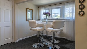 Une pièce comprenant deux fauteuils en cuir blanc, une petite table, un miroir et une fenêtre avec des rideaux.