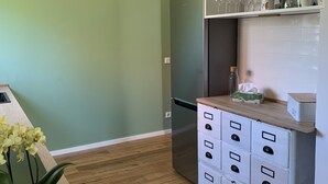 A kitchen with a green wall, wooden floor, white cabinets, and a built-in refrigerator. - Idyllische Ferienwohnung in Potsdam (Potsdam)