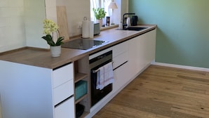 A modern kitchen with white cabinetry, a wooden countertop, a built-in oven, and a window providing natural light. - Idyllische Ferienwohnung in Potsdam (Potsdam)