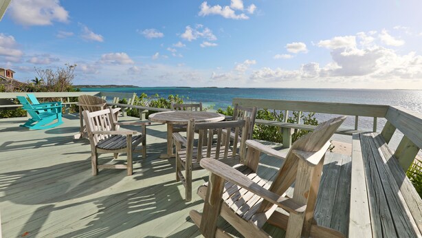 Une terrasse en bois, aménagée avec du mobilier d’extérieur, donnant sur une étendue d’eau.