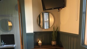 Une chambre avec un lit, une table de chevet avec une bougie, un miroir, un téléviseur fixé au mur et une salle de bain avec un lavabo et un miroir.
