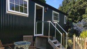 Un petit bâtiment avec un escalier menant à une porte, une table et des chaises à l’extérieur.