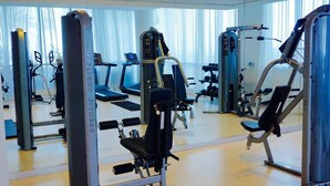 A gym with various exercise machines, a mirrored wall, and a treadmill in the background.