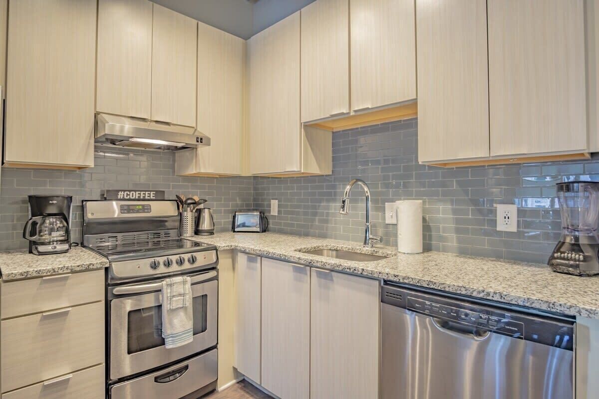 A modern kitchen with stainless steel appliances, a granite countertop, and light-colored cabinetry.