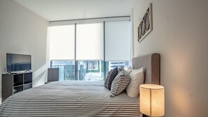 A modern bedroom with a large bed, a TV, a lamp, and a window with blinds. - 3380 Peachtree Rd NE Atlanta, GA 30326, USA (Atlanta)
