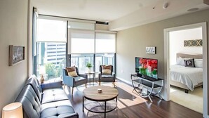 A modern living room with a sofa, two armchairs, a coffee table, a TV, and a bed with a pillow marked 'P'. - 3380 Peachtree Rd NE Atlanta, GA 30326, USA (Atlanta)