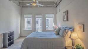 Una camera da letto con un letto, una ventola a soffitto, un comodino, una lampada e una finestra.
