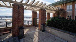 Een dakterras met een pergola, bakstenen pilaren, uitzicht op het water en een gebouw met een glazen gevel.