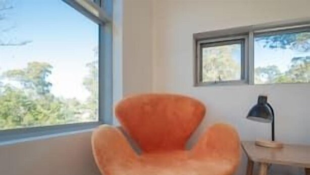 A room with a large window, a wooden desk, and an orange chair.