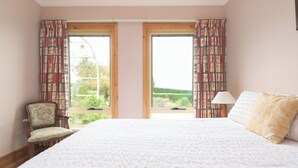 A bedroom with a large bed, two windows with curtains, a chair, and a bedside lamp. - Rural Apartment with Stunning Views! (Relbia)