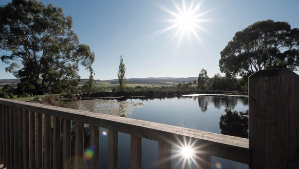 A wooden deck overlooking a calm lake with trees and hills in the background. - Rural Apartment with Stunning Views! (Relbia)