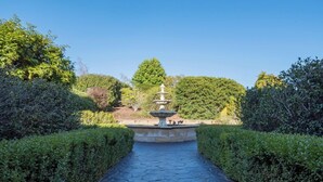 A stone pathway leading to a tiered fountain in a well-manicured garden with neatly trimmed hedges. - Rural Apartment with Stunning Views! (Relbia)