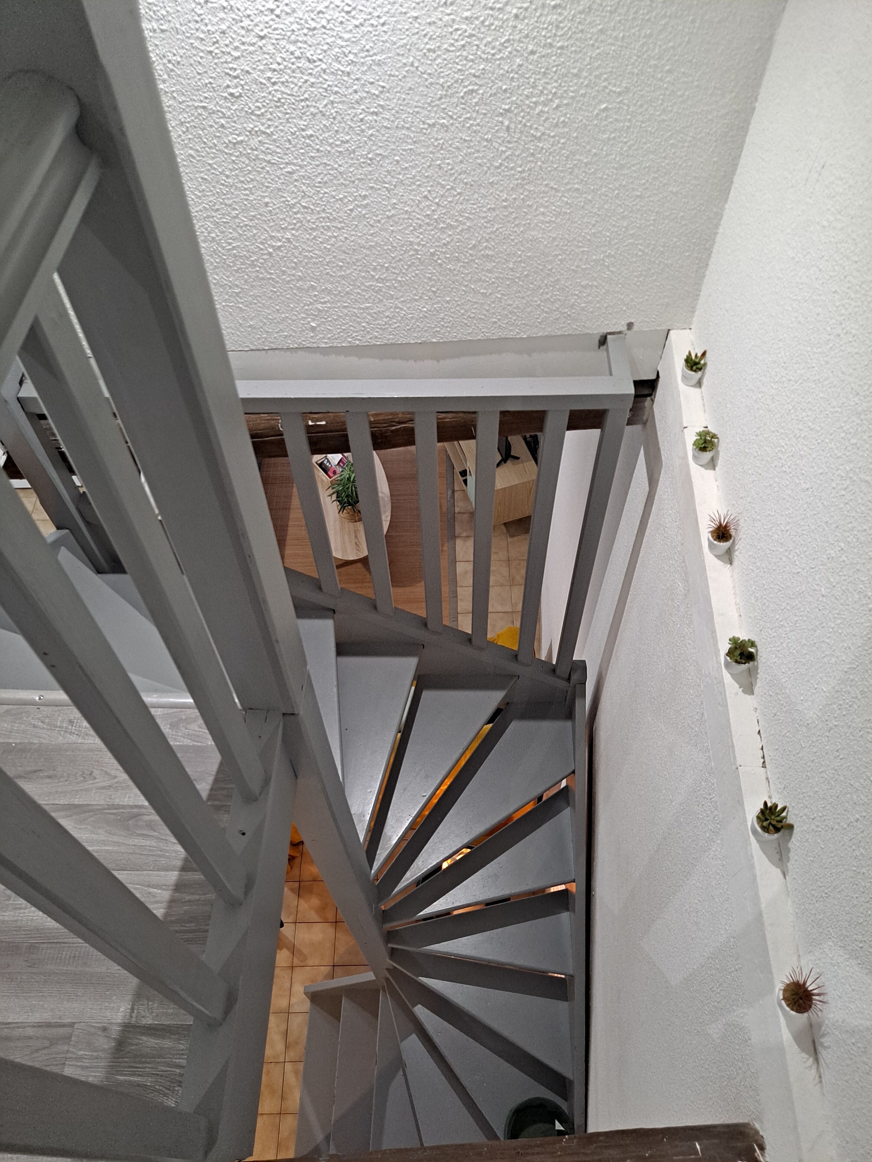 Eine Treppe mit grauer Geländer und einer weißen Wand mit Blumentöpfen.