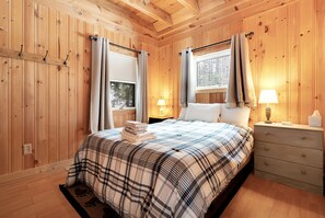 A wooden-paneled bedroom with a bed, nightstands, and a window.