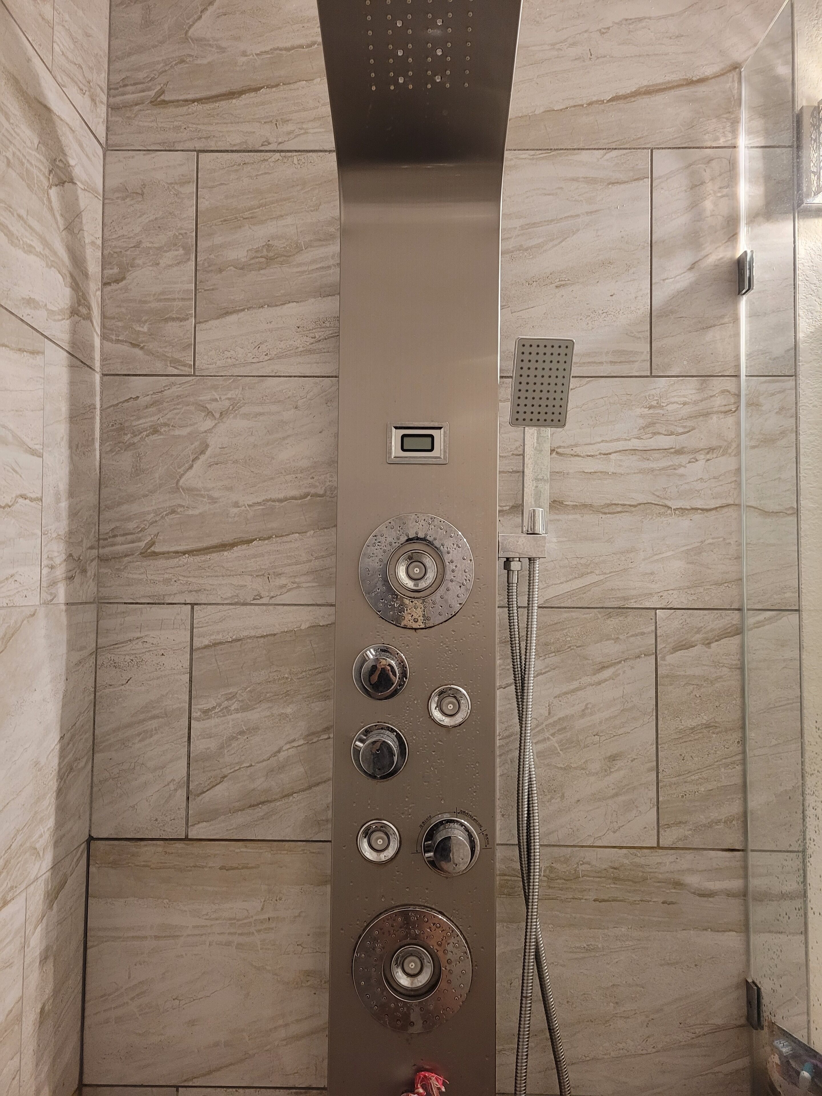 A modern shower with multiple controls and a handheld showerhead, set against a backdrop of marble tiles.