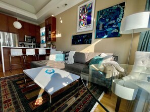 A modern living room with a sofa, a glass coffee table, and a kitchen area in the background.