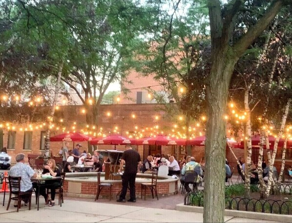 Enjoy meals under the shade of red umbrellas in a serene outdoor dining area surrounded by trees and a fence.