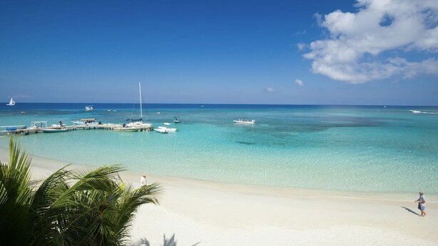 A beach with clear turquoise water, boats docked at a pier, and a sandy shore. - $3,000,000 Luxury Beach Front (4) Bedrooms Condo famous West Bay Beach Sleeps 8 (West Bay)