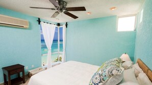 A bedroom with a bed, a ceiling fan, a window with a view of the ocean, and a small table. - $3,000,000 Luxury Beach Front (4) Bedrooms Condo famous West Bay Beach Sleeps 8 (West Bay)