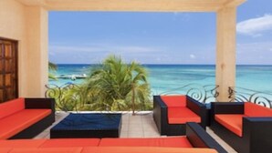 A covered outdoor seating area with red and black cushions, a view of the ocean, and a palm tree. - $3,000,000 Luxury Beach Front (4) Bedrooms Condo famous West Bay Beach Sleeps 8 (West Bay)