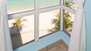 A room with a large window offering a view of a beach with clear blue water and a sandy shore. - $3,000,000 Luxury Beach Front (4) Bedrooms Condo famous West Bay Beach Sleeps 8 (West Bay)