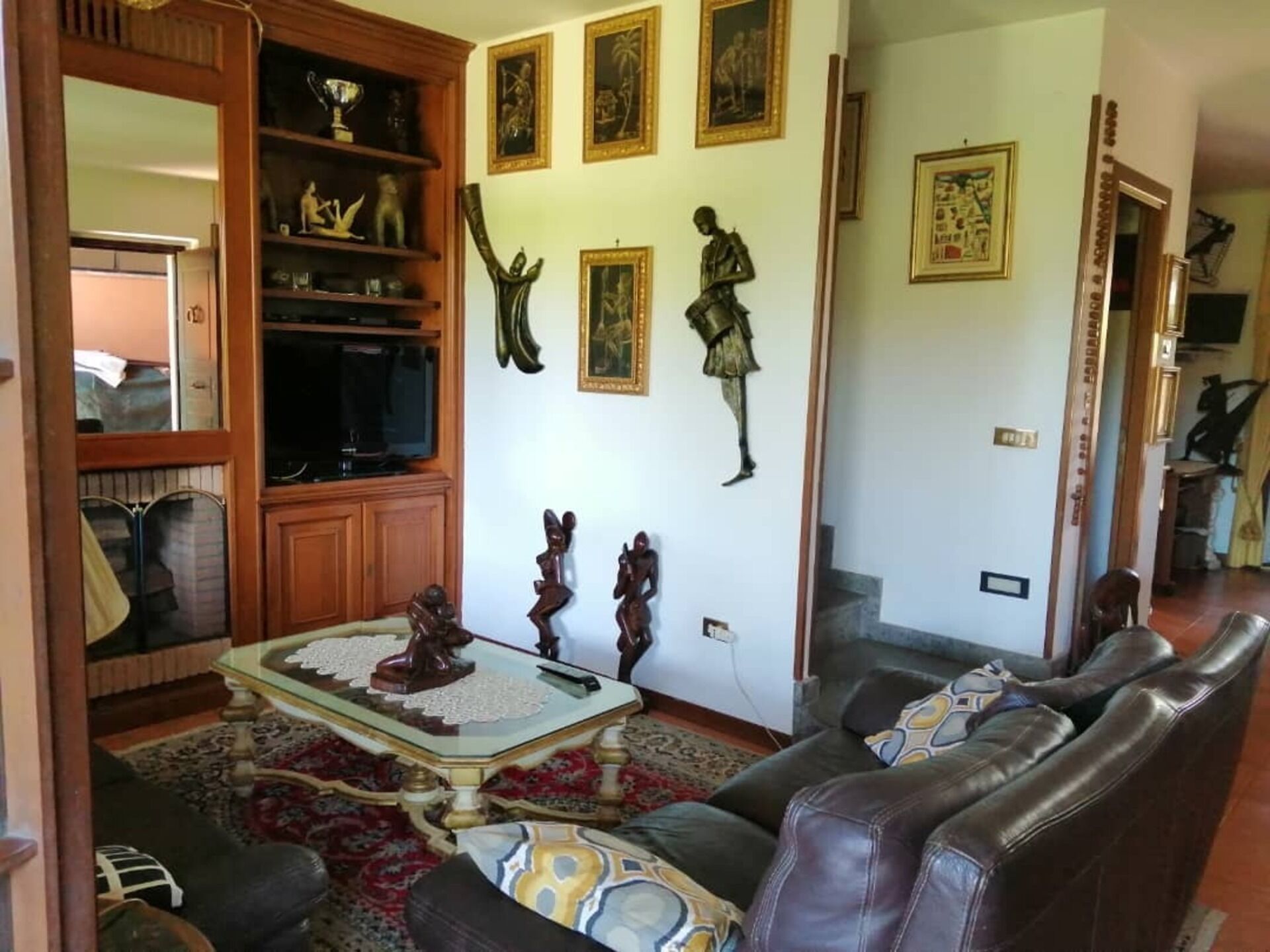 A living room with a wooden cabinet, a glass-top coffee table, leather sofas, and wall-mounted artwork.