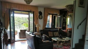 Un salon avec un canapé, une table basse et une lampe. Il y a une fenêtre avec des rideaux, une horloge au mur et un escalier menant à une autre pièce.
