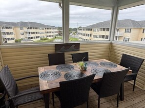 Une terrasse couverte, avec une table en bois et des chaises en osier noir, donnant sur un quartier résidentiel composé d’immeubles d’appartements.