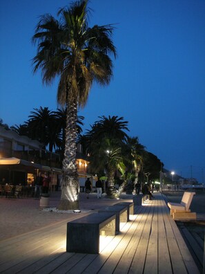 A wooden boardwalk with benches, palm trees, and outdoor seating areas. - Hotel Bergamo Mare Mhotelsgroup (San Bartolomeo al Mare)