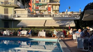 Un espace aménagé autour de la piscine, avec des sièges et des tables en plein air, entouré d’immeubles dotés de balcons et de terrasses.