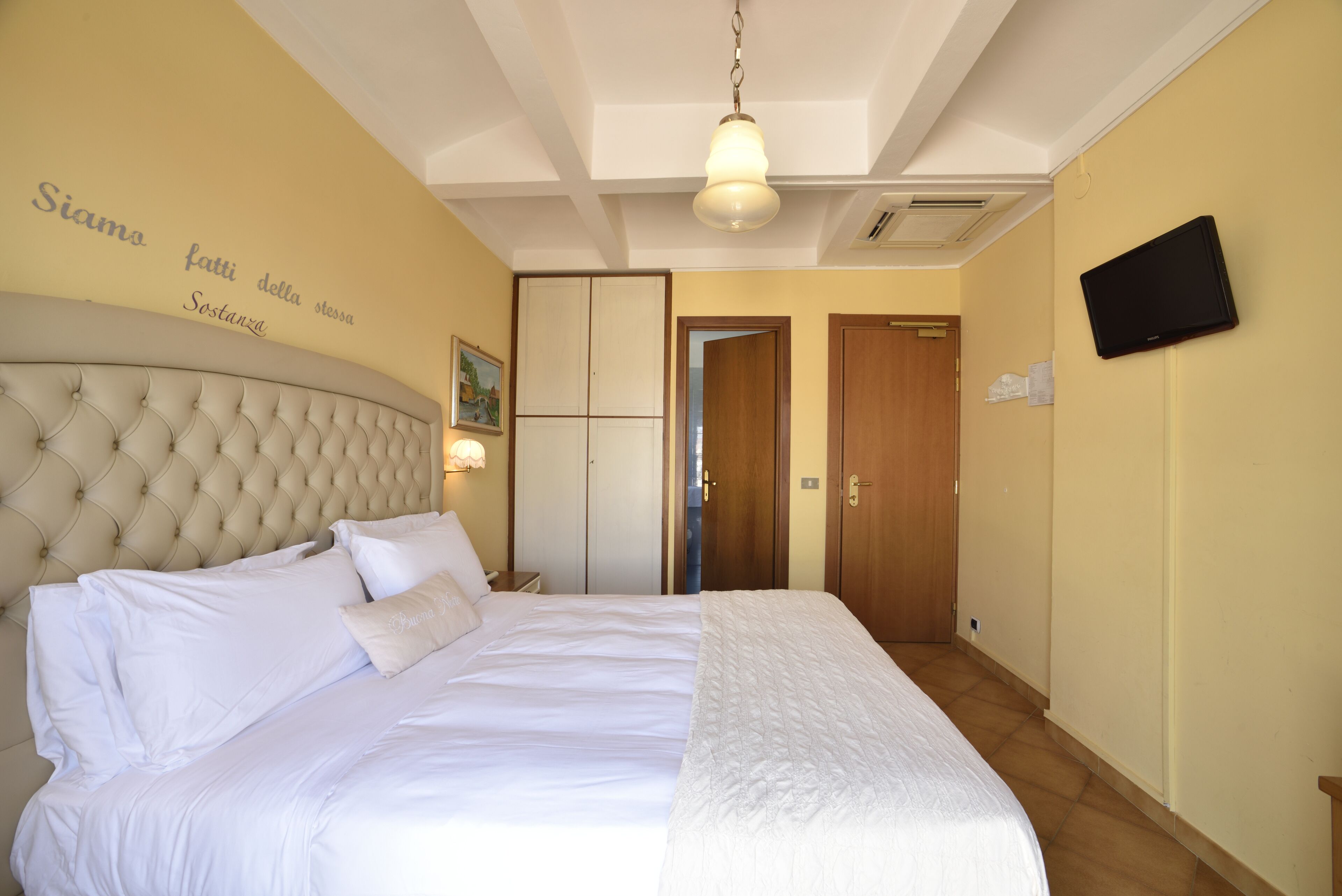 A neatly made bed with white linens, a tufted headboard, and a wall-mounted television.