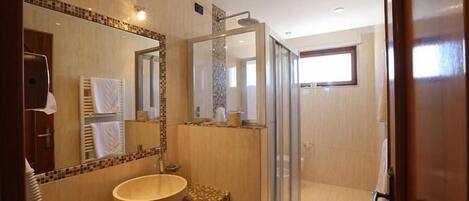 A modern bathroom with a large mirror, a wooden vanity, a glass shower enclosure, and a view of the adjacent room.