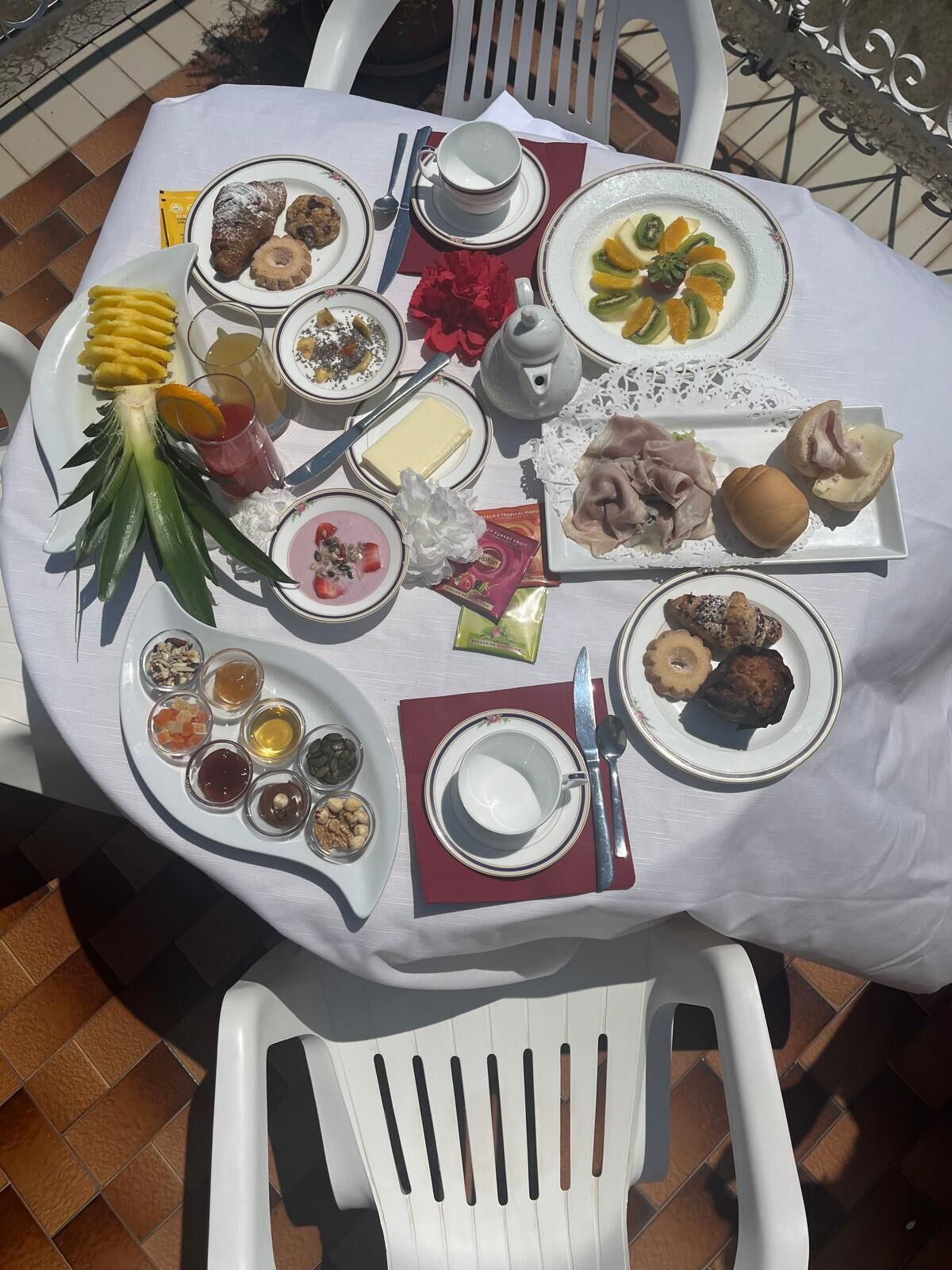 A table set with various dishes, including fruits, pastries, and condiments, on an outdoor patio.