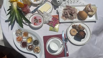 A table set with various dishes, including fruits, pastries, and condiments, on an outdoor patio.