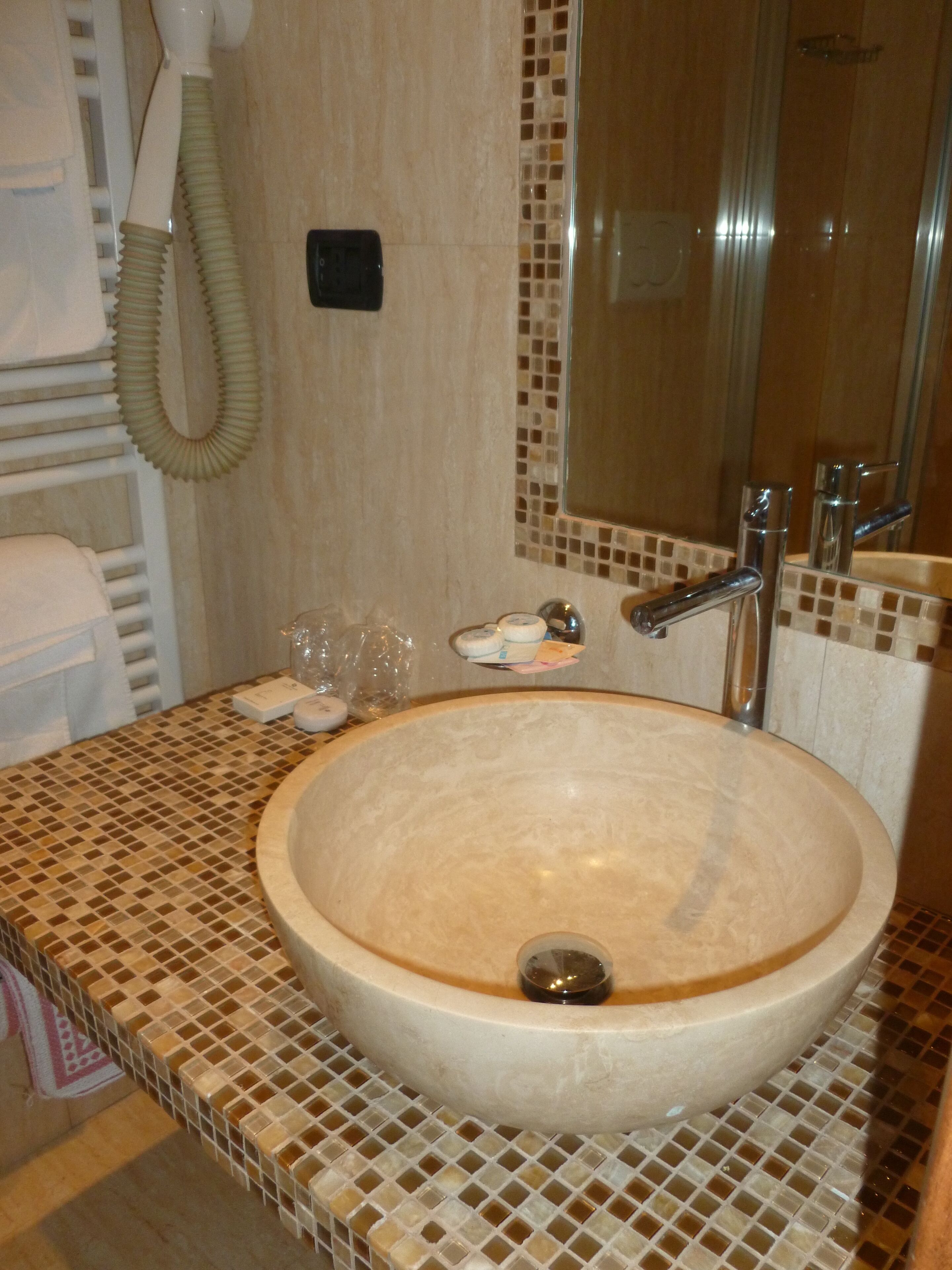 A bathroom with a large beige sink, a mirror, and a towel rack.