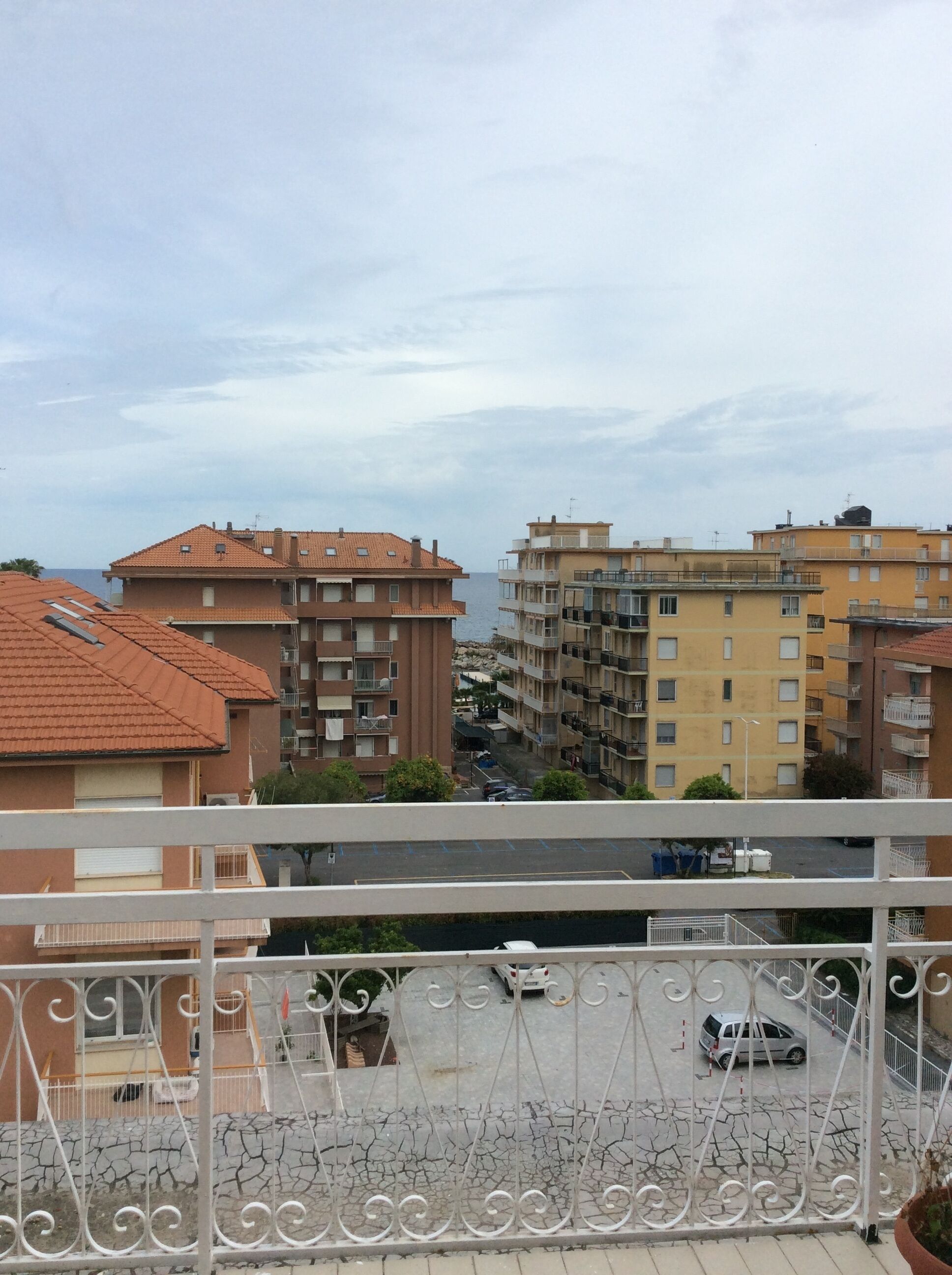 A residential area with multi-story buildings, a street with parked cars, and a view of the sea.