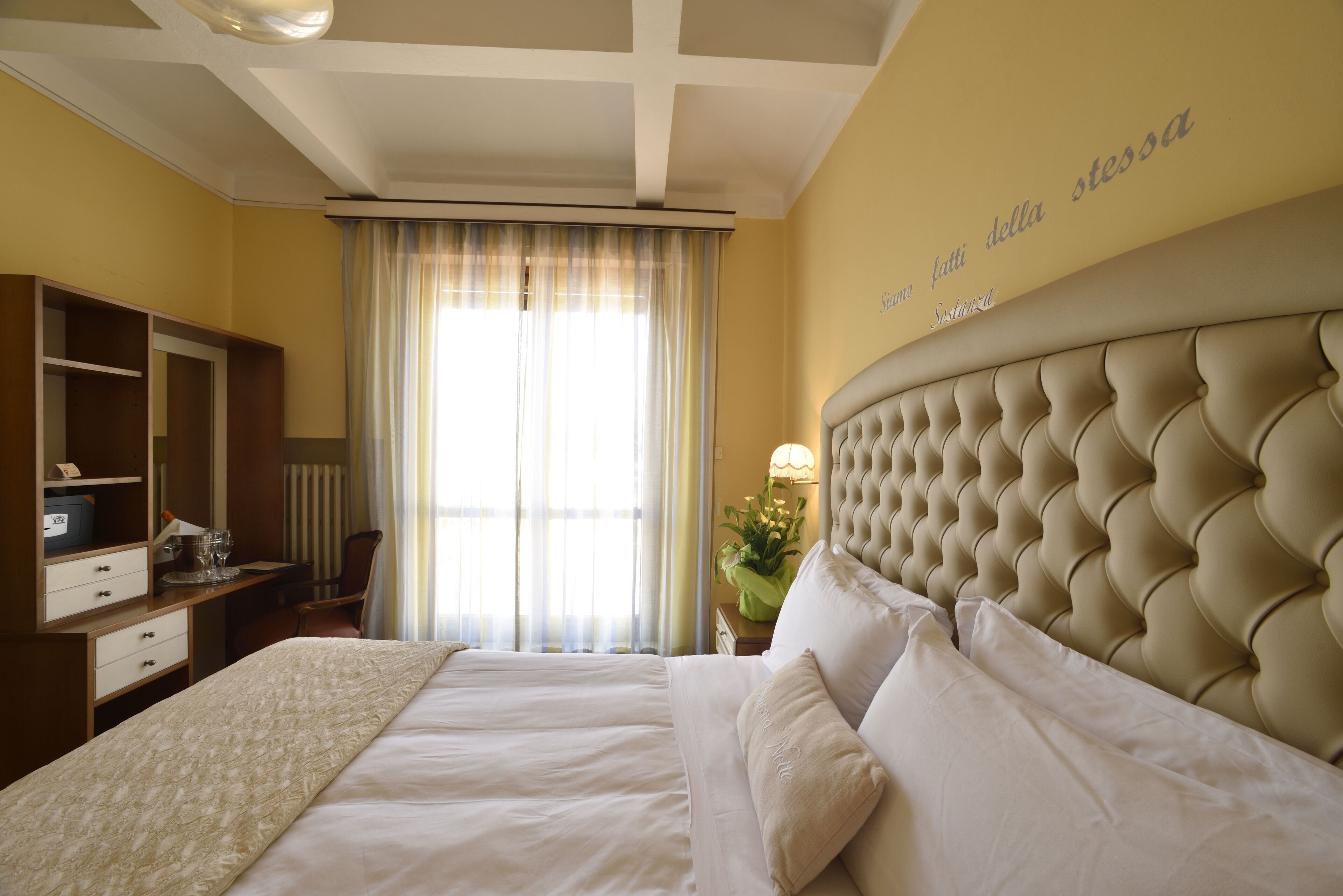 A hotel room with a large bed, a desk with a chair, a wardrobe, and a window with curtains.
