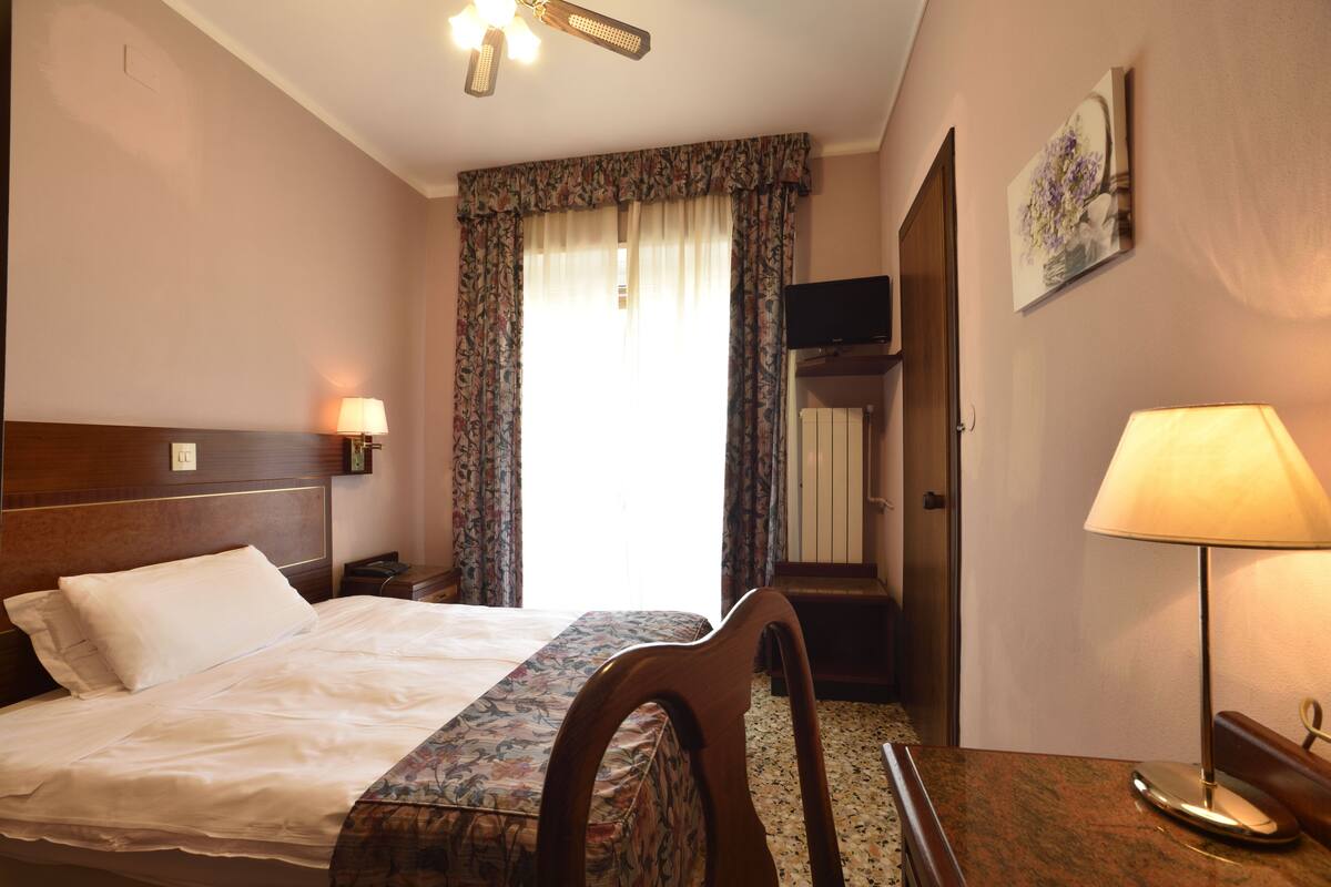 Una habitación de hotel con cama, escritorio, silla, televisor y puerta.