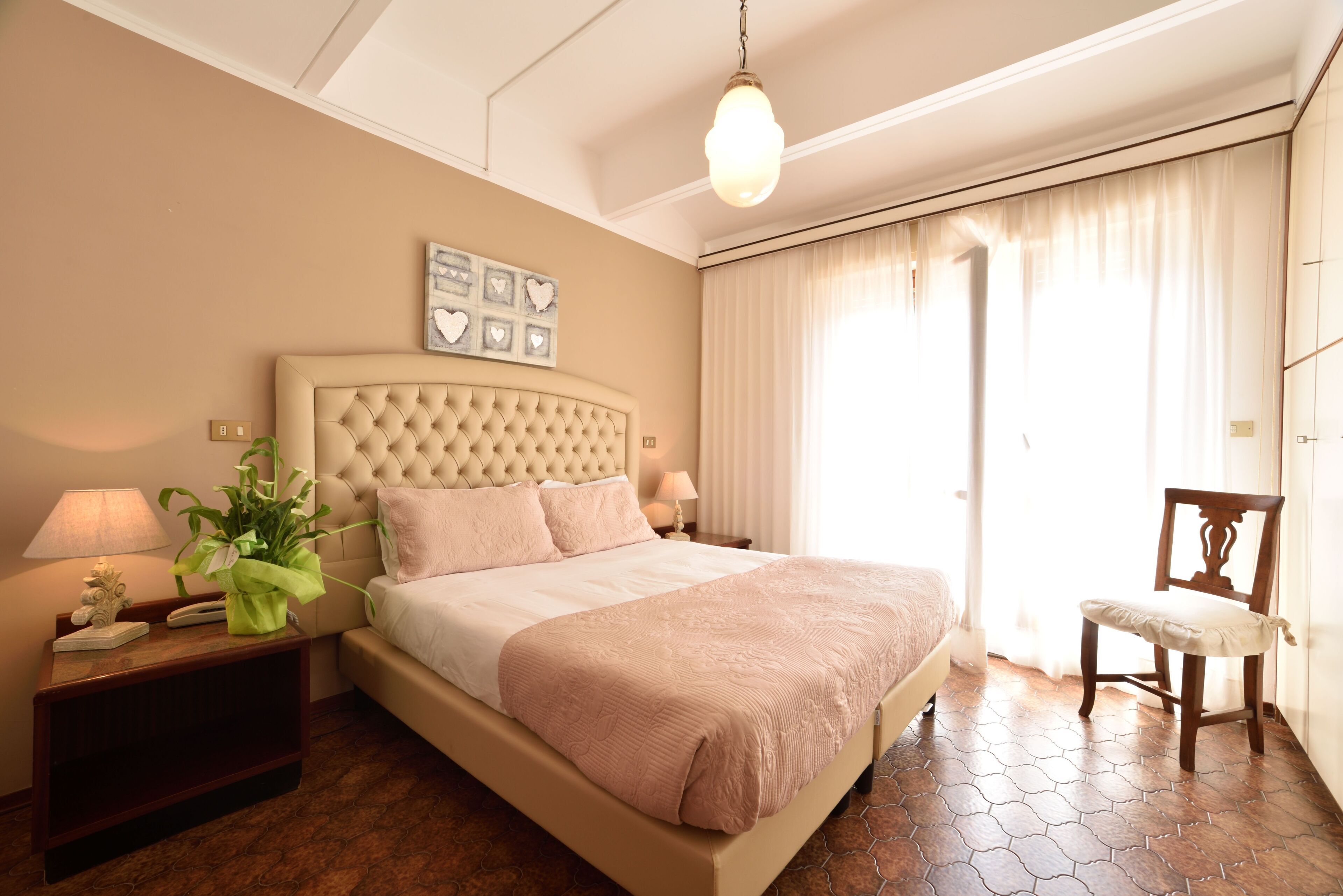 A neatly arranged bedroom with a tufted headboard, a large bed, a bedside table with a lamp, and a chair.