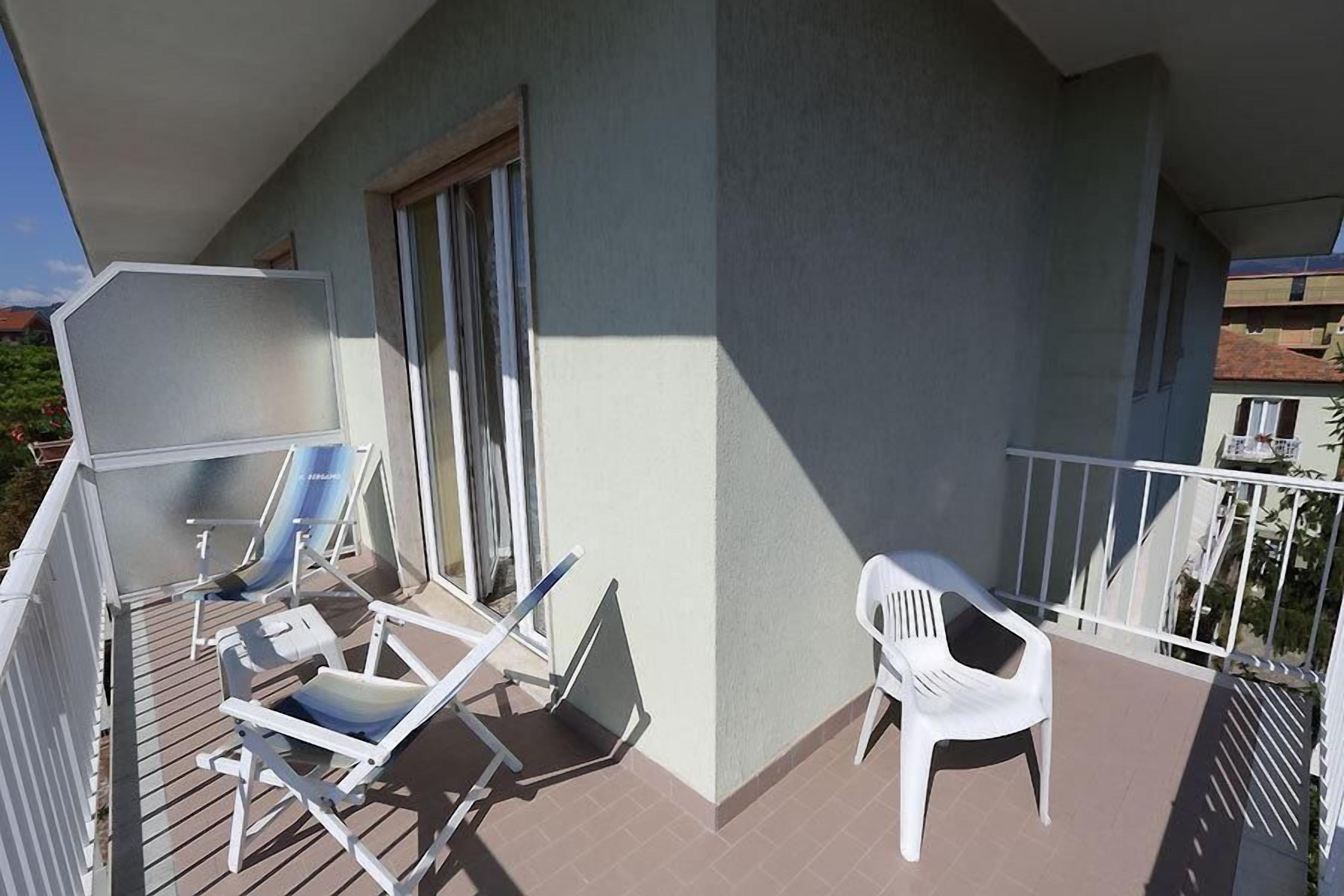 Un balcón con dos sillones de descanso, una silla de plástico blanco y un ventanal corredero.