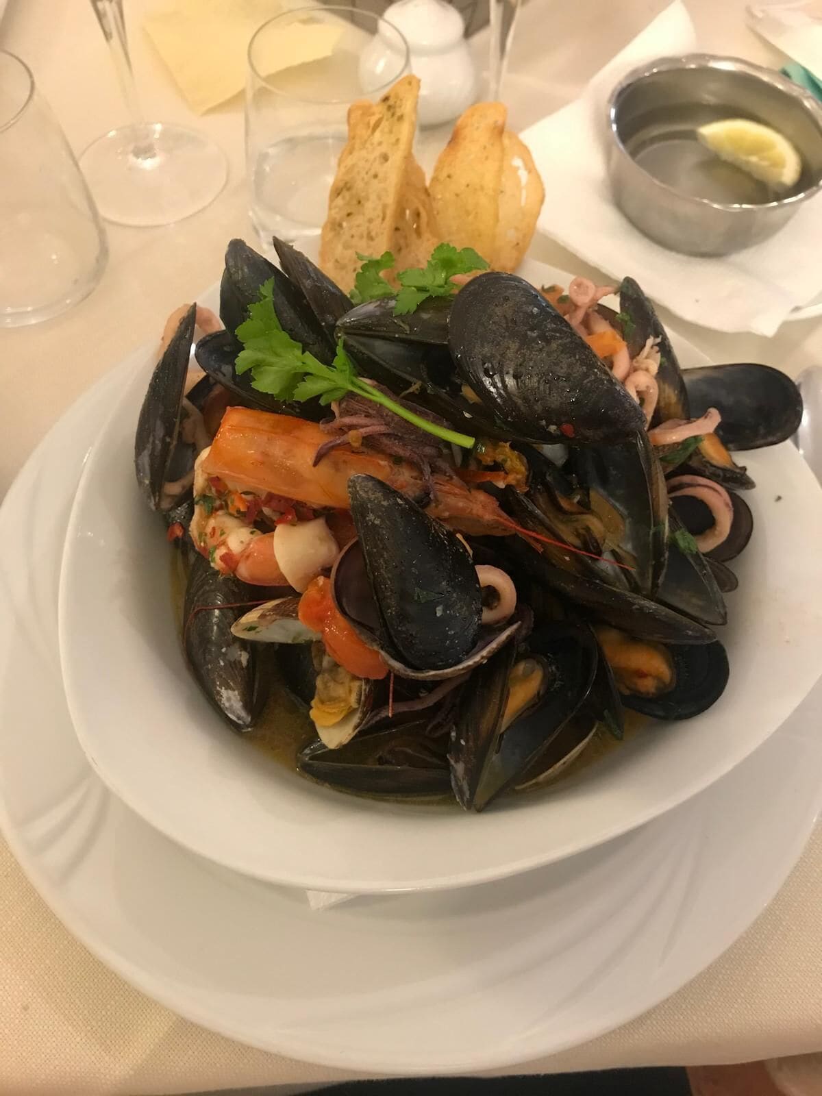Un plat de fruits de mer comprenant des moules, des crevettes et d’autres fruits de mer, servi dans une assiette blanche.