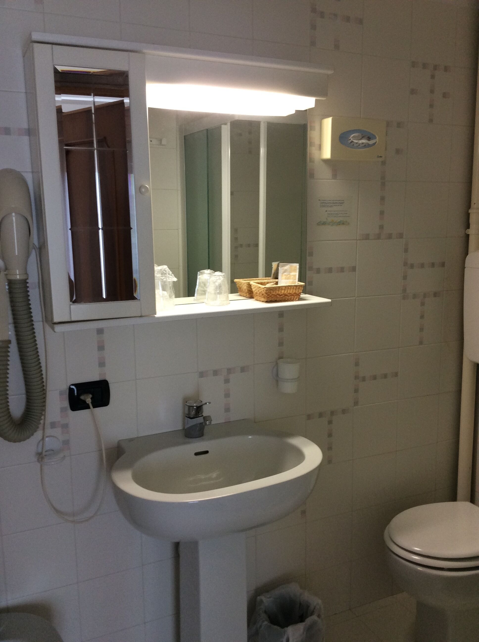 A bathroom with a white sink, a mirror above it, a telephone, and a toilet.