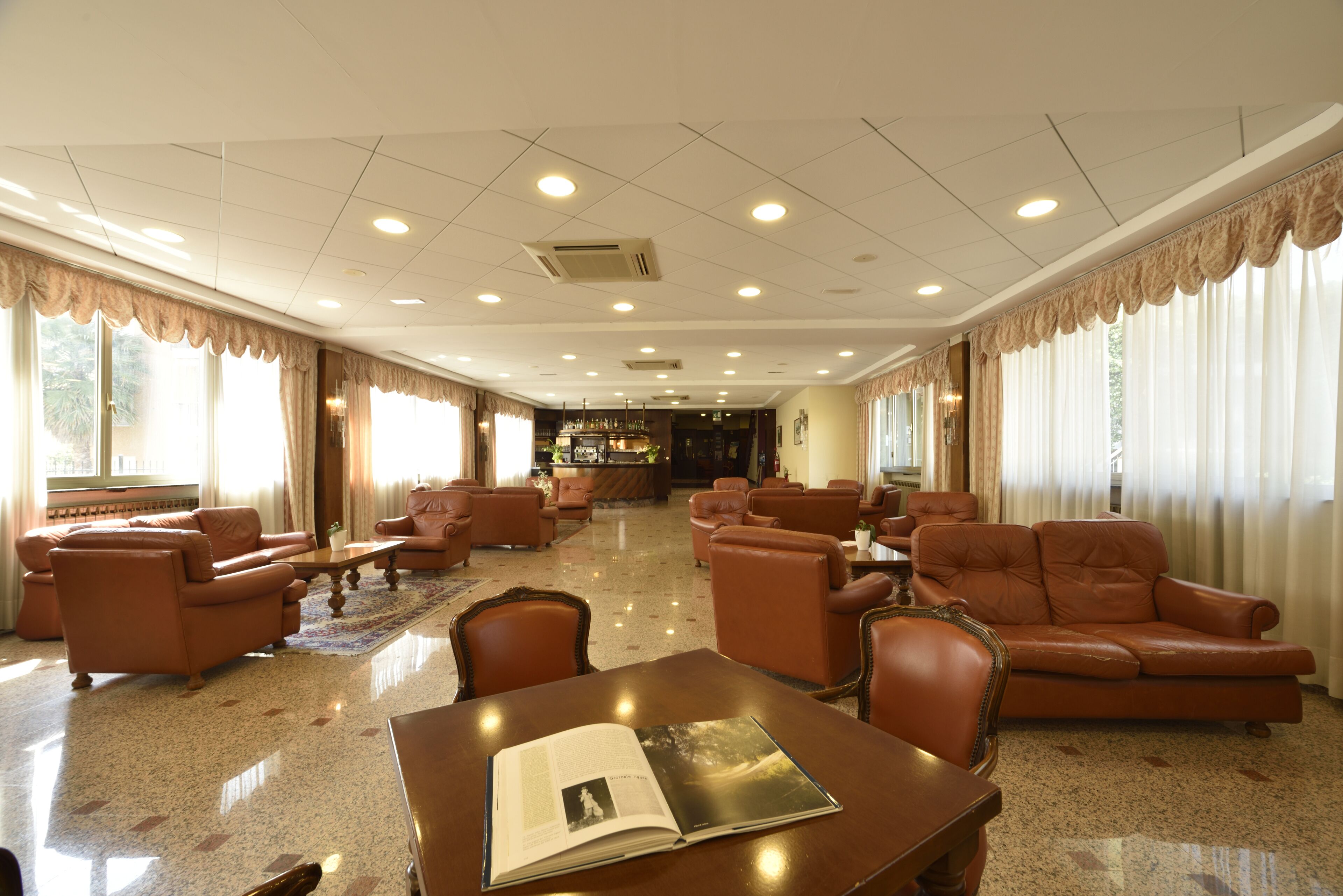 Un hall d’entrée spacieux, avec des canapés en cuir, une table basse en bois et un bar situé au fond de la pièce.