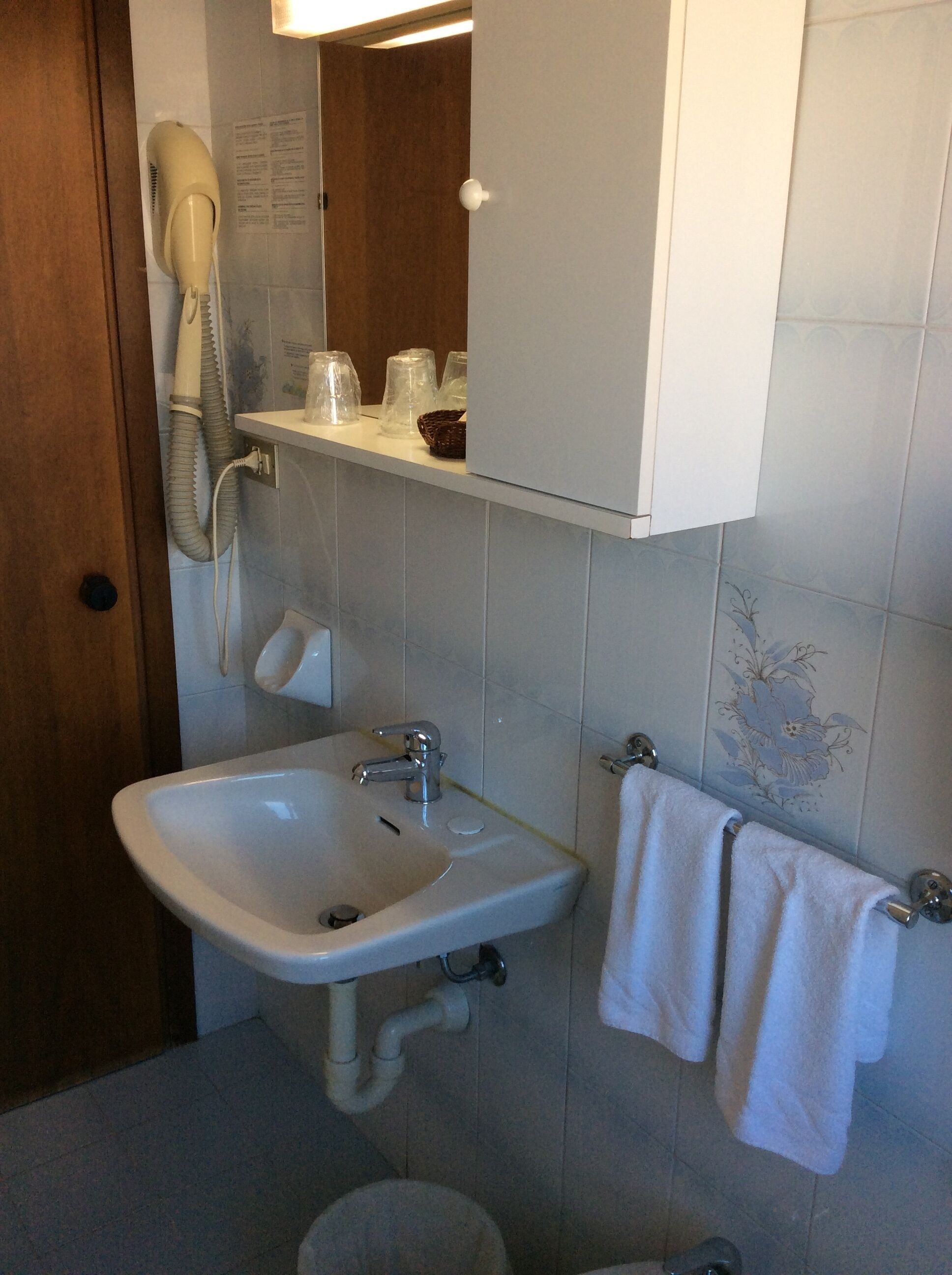 Een badkamer met een wastafel, spiegel, handdoekhouder en een haardroger op een wandplank.